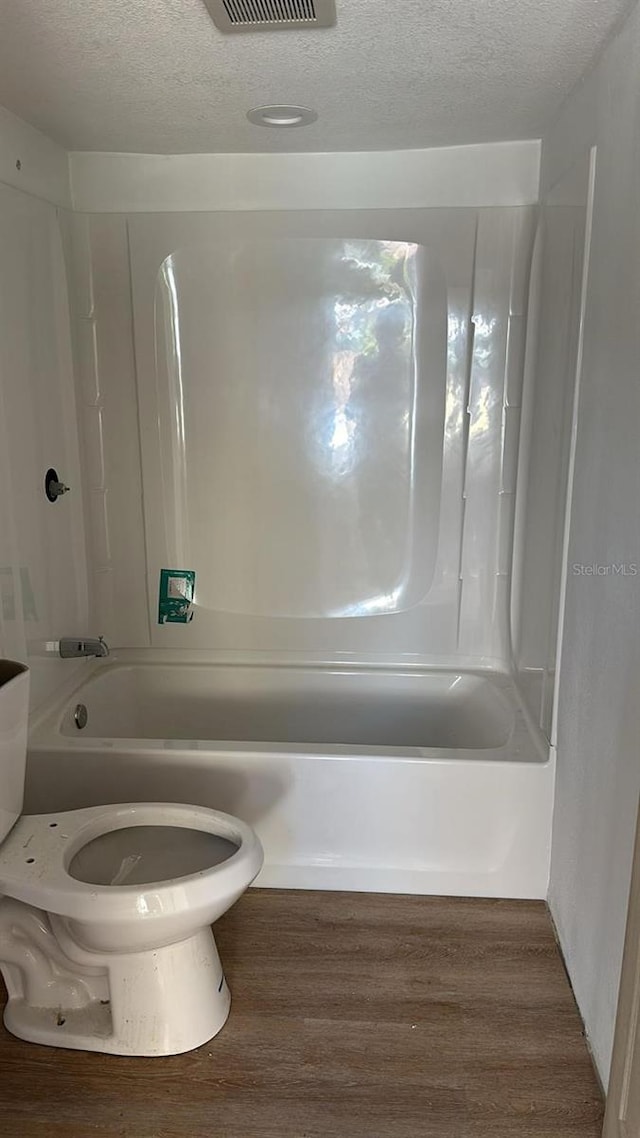 bathroom with toilet, bathtub / shower combination, a textured ceiling, and hardwood / wood-style floors