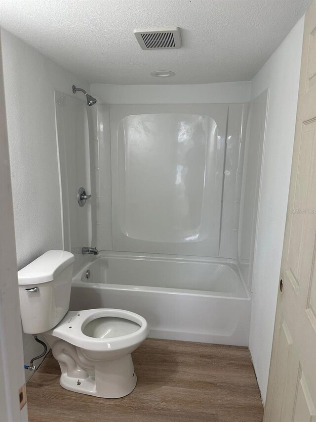 bathroom with a textured ceiling, wood-type flooring, toilet, and shower / bath combination