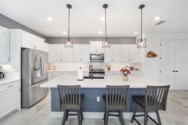 kitchen featuring white cabinets, appliances with stainless steel finishes, an island with sink, and hanging light fixtures