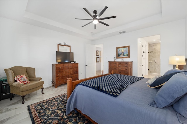 bedroom with ensuite bath, a raised ceiling, and ceiling fan