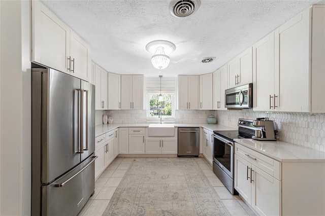 kitchen featuring sink, white cabinets, light tile patterned floors, appliances with stainless steel finishes, and a textured ceiling