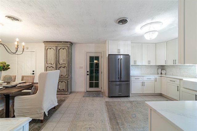 kitchen with stainless steel fridge, white cabinets, backsplash, a textured ceiling, and a chandelier