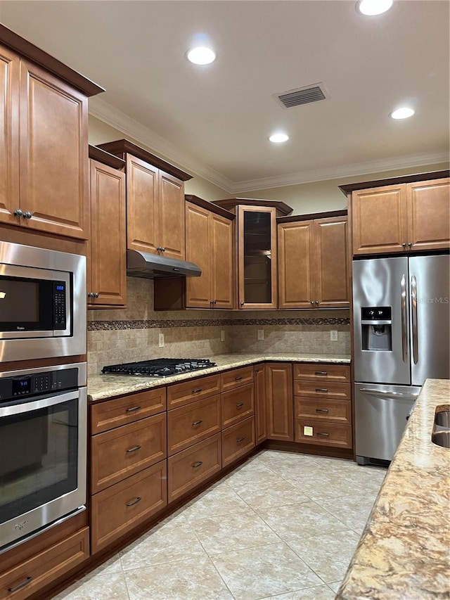 kitchen with tasteful backsplash, light stone countertops, appliances with stainless steel finishes, crown molding, and light tile patterned floors