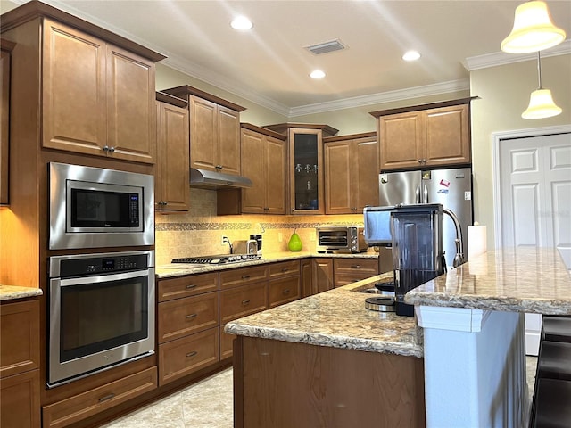 kitchen with light stone countertops, hanging light fixtures, stainless steel appliances, ornamental molding, and a center island with sink