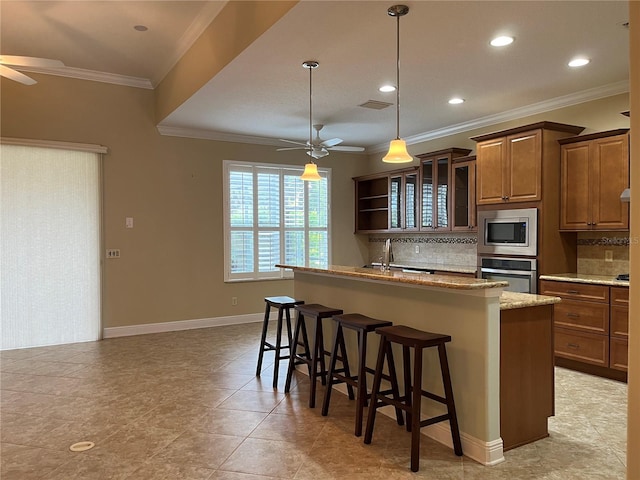 kitchen with appliances with stainless steel finishes, an island with sink, ceiling fan, decorative backsplash, and a breakfast bar