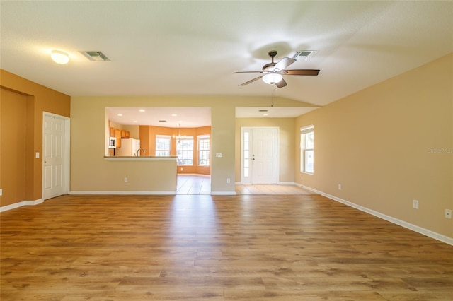 unfurnished living room with ceiling fan with notable chandelier, a healthy amount of sunlight, and light wood-type flooring