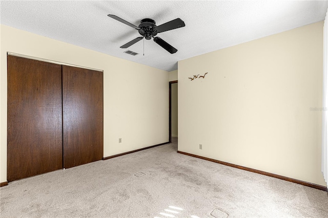 unfurnished bedroom featuring ceiling fan, light colored carpet, a closet, and a textured ceiling