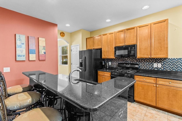 kitchen with black appliances, dark stone countertops, a kitchen breakfast bar, an island with sink, and backsplash