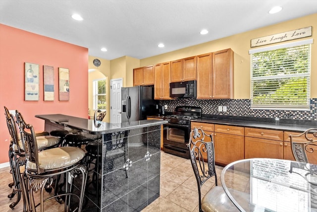 kitchen featuring light tile patterned flooring, backsplash, a kitchen breakfast bar, and black appliances