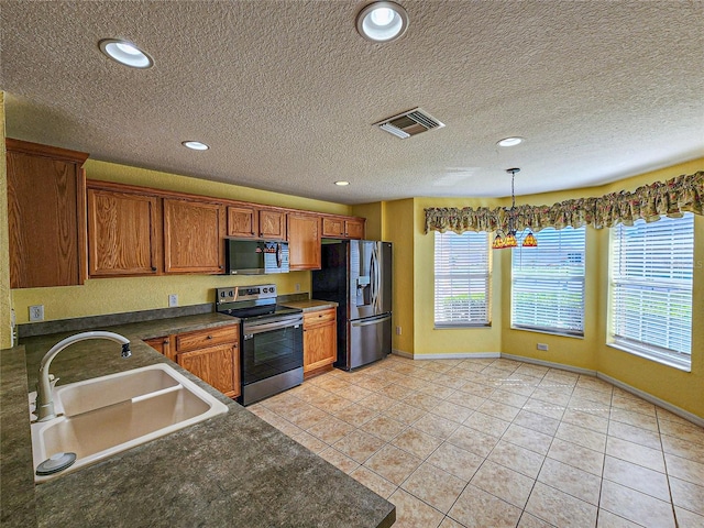 kitchen featuring hanging light fixtures, light tile patterned floors, a textured ceiling, stainless steel appliances, and sink