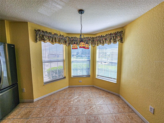 unfurnished dining area featuring a healthy amount of sunlight, a textured ceiling, tile patterned floors, and an inviting chandelier