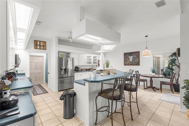 kitchen with white cabinets, a kitchen breakfast bar, stainless steel appliances, dark countertops, and light tile patterned floors