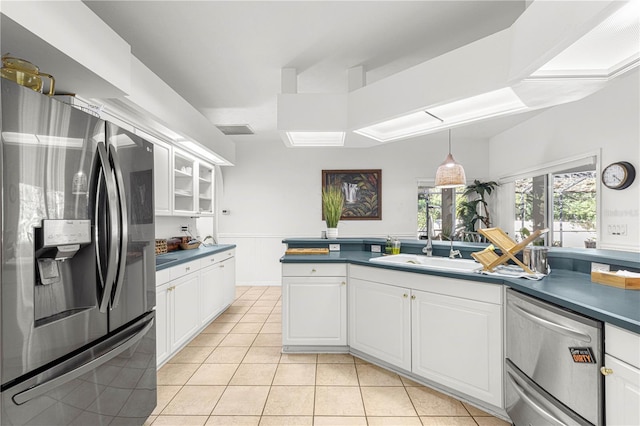 kitchen featuring dark countertops, light tile patterned floors, a sink, appliances with stainless steel finishes, and white cabinetry
