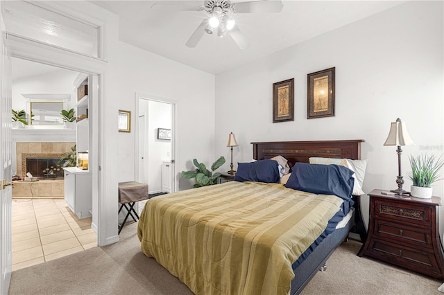 bedroom with light colored carpet, ceiling fan, a tile fireplace, ensuite bath, and light tile patterned floors