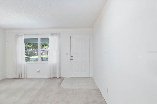 empty room with light carpet, a textured ceiling, and ornamental molding