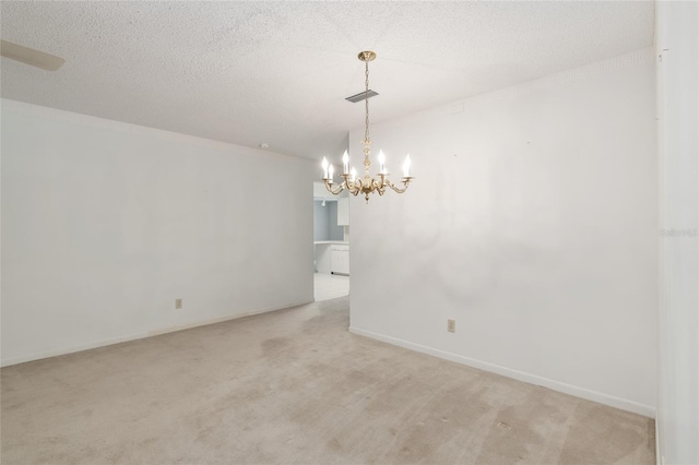 empty room with a textured ceiling, a chandelier, and light colored carpet