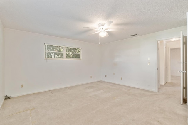 spare room with a textured ceiling, light colored carpet, and ceiling fan