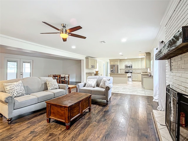 living room featuring ceiling fan, wood-type flooring, a fireplace, crown molding, and sink