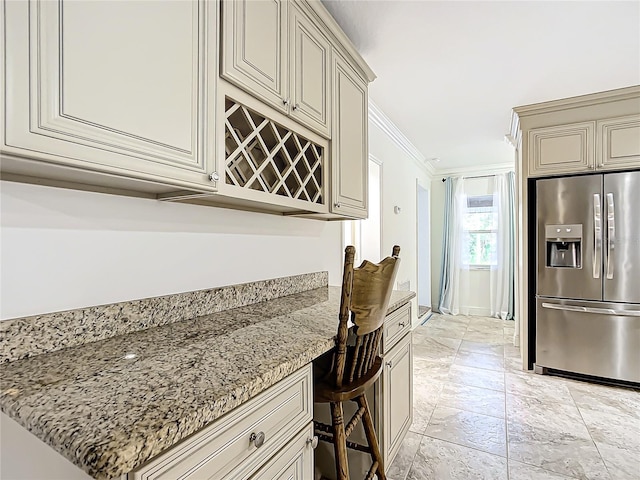 kitchen with ornamental molding, light stone countertops, stainless steel refrigerator with ice dispenser, and cream cabinets