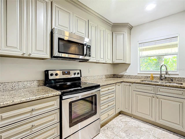 kitchen with light stone countertops, appliances with stainless steel finishes, sink, cream cabinetry, and light tile patterned floors