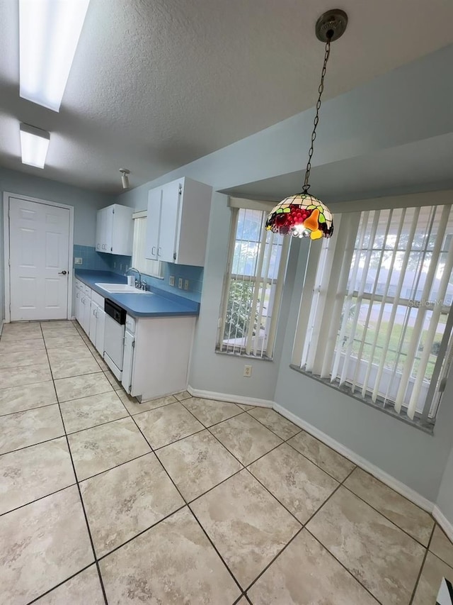 kitchen featuring hanging light fixtures, white dishwasher, sink, light tile patterned floors, and white cabinetry