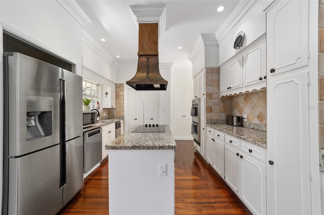 kitchen with appliances with stainless steel finishes, a center island, white cabinetry, light stone counters, and ornamental molding