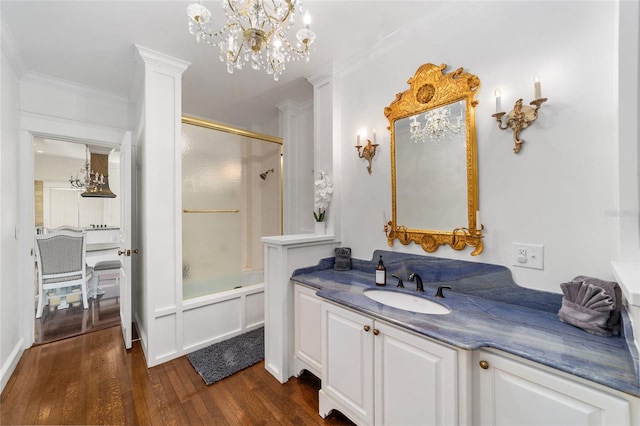 bathroom with bath / shower combo with glass door, an inviting chandelier, hardwood / wood-style flooring, vanity, and crown molding