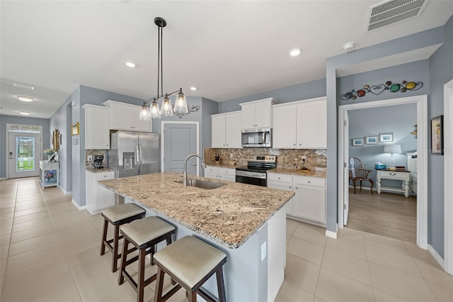 kitchen with white cabinetry, sink, stainless steel appliances, light stone counters, and a center island with sink