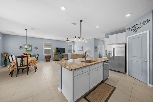 kitchen with light stone countertops, appliances with stainless steel finishes, sink, white cabinets, and an island with sink