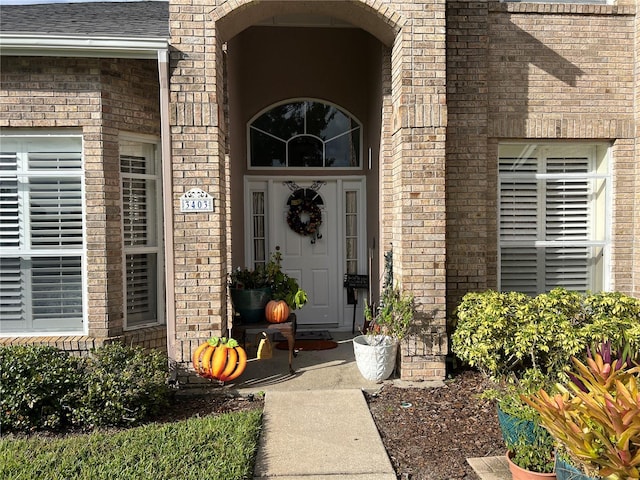 property entrance featuring a shingled roof and brick siding