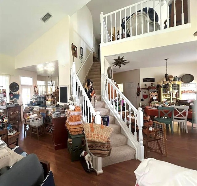 living area featuring a chandelier, visible vents, stairway, wood finished floors, and high vaulted ceiling