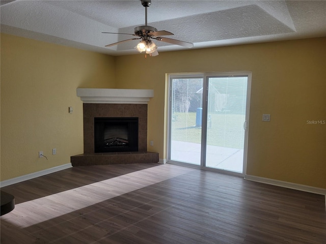 unfurnished living room with a tiled fireplace, a textured ceiling, dark hardwood / wood-style flooring, and ceiling fan