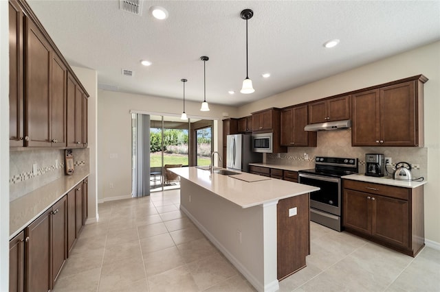 kitchen featuring hanging light fixtures, stainless steel appliances, a center island with sink, and backsplash