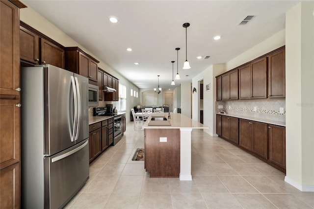 kitchen featuring a center island with sink, stainless steel appliances, sink, dark brown cabinetry, and decorative light fixtures