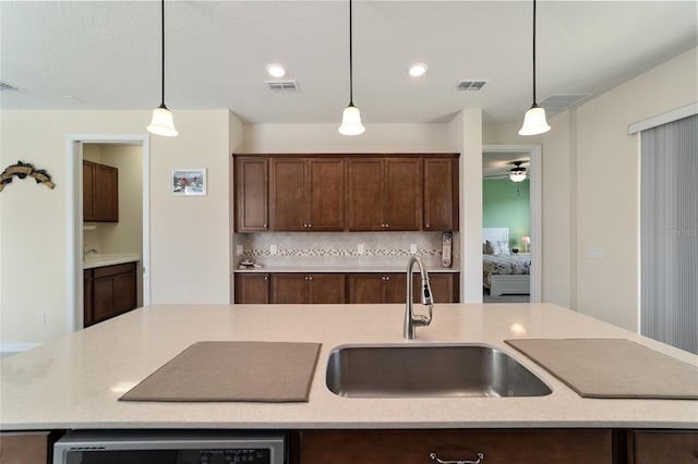 kitchen featuring decorative backsplash, dark brown cabinets, an island with sink, pendant lighting, and sink