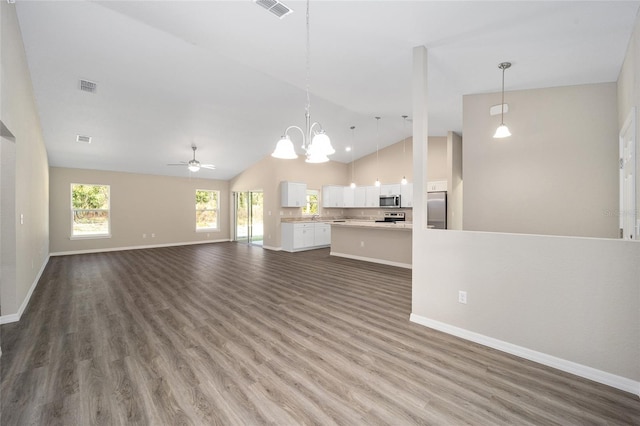 unfurnished living room featuring high vaulted ceiling, dark hardwood / wood-style floors, and ceiling fan with notable chandelier