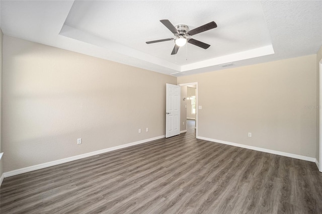 unfurnished room featuring dark wood-type flooring, a tray ceiling, a textured ceiling, and ceiling fan