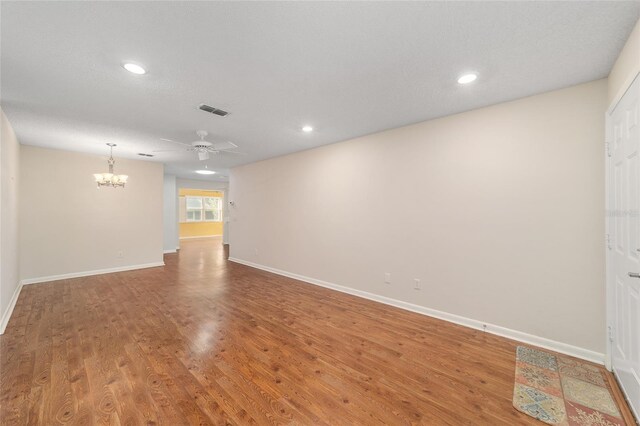 spare room with a textured ceiling, wood-type flooring, and ceiling fan with notable chandelier