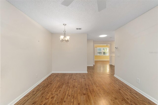 spare room featuring a textured ceiling, wood-type flooring, and ceiling fan with notable chandelier