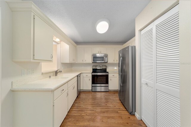 kitchen with sink, appliances with stainless steel finishes, a textured ceiling, and light wood-type flooring