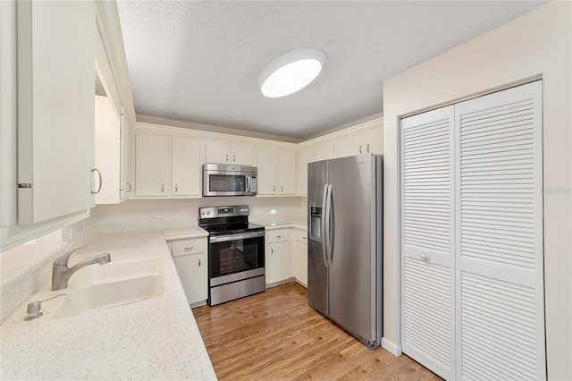 kitchen featuring white cabinets, appliances with stainless steel finishes, a textured ceiling, light wood-type flooring, and sink