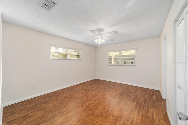 unfurnished bedroom with ceiling fan, a textured ceiling, multiple windows, and dark hardwood / wood-style flooring