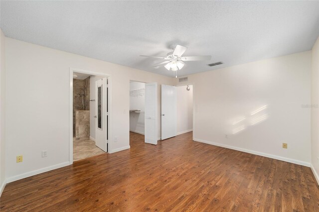 unfurnished bedroom with a spacious closet, a textured ceiling, dark hardwood / wood-style flooring, a closet, and ceiling fan