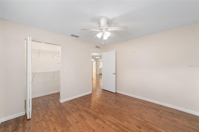 unfurnished bedroom featuring a walk in closet, a textured ceiling, a closet, ceiling fan, and dark hardwood / wood-style floors