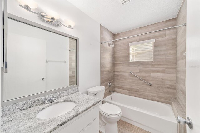 full bathroom featuring toilet, wood-type flooring, tiled shower / bath, vanity, and a textured ceiling