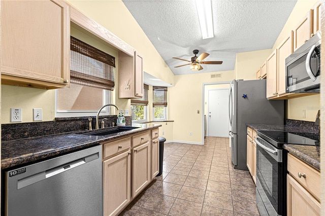 kitchen with appliances with stainless steel finishes, sink, light brown cabinetry, a textured ceiling, and vaulted ceiling