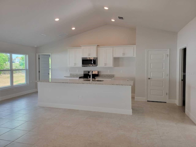 kitchen with appliances with stainless steel finishes, white cabinetry, lofted ceiling, light stone counters, and a center island with sink