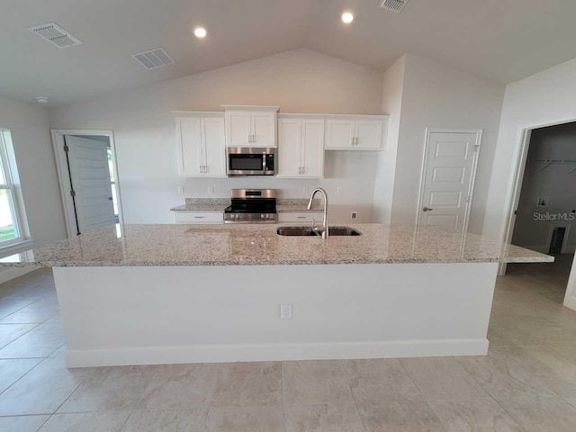 kitchen with appliances with stainless steel finishes, sink, a large island, vaulted ceiling, and light stone counters