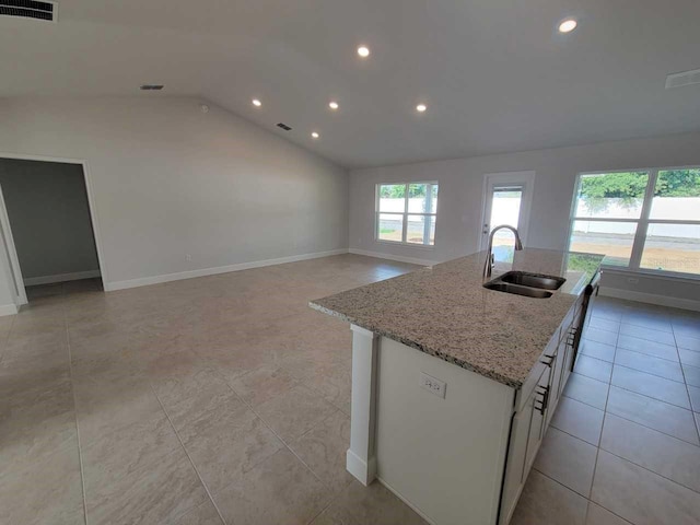 kitchen with an island with sink, sink, light stone countertops, vaulted ceiling, and light tile patterned floors