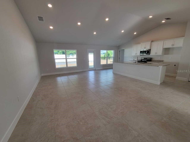 kitchen with lofted ceiling, white cabinets, a center island with sink, appliances with stainless steel finishes, and light stone countertops